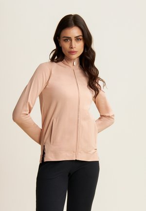 Veste zippée rose clair avec un col montant, des manches longues, des poches latérales et des accents latéraux noirs. Tissu lisse et extensible avec une coupe ajustée.