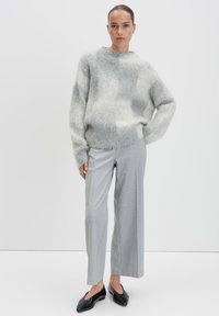 Helles graues, flauschiges Sweatshirt mit rundem Halsausschnitt; kombiniert mit maßgeschneiderten, hellgrauen Hosen und schwarzen Ballerinas. Weiche Texturen und lässige Passform.