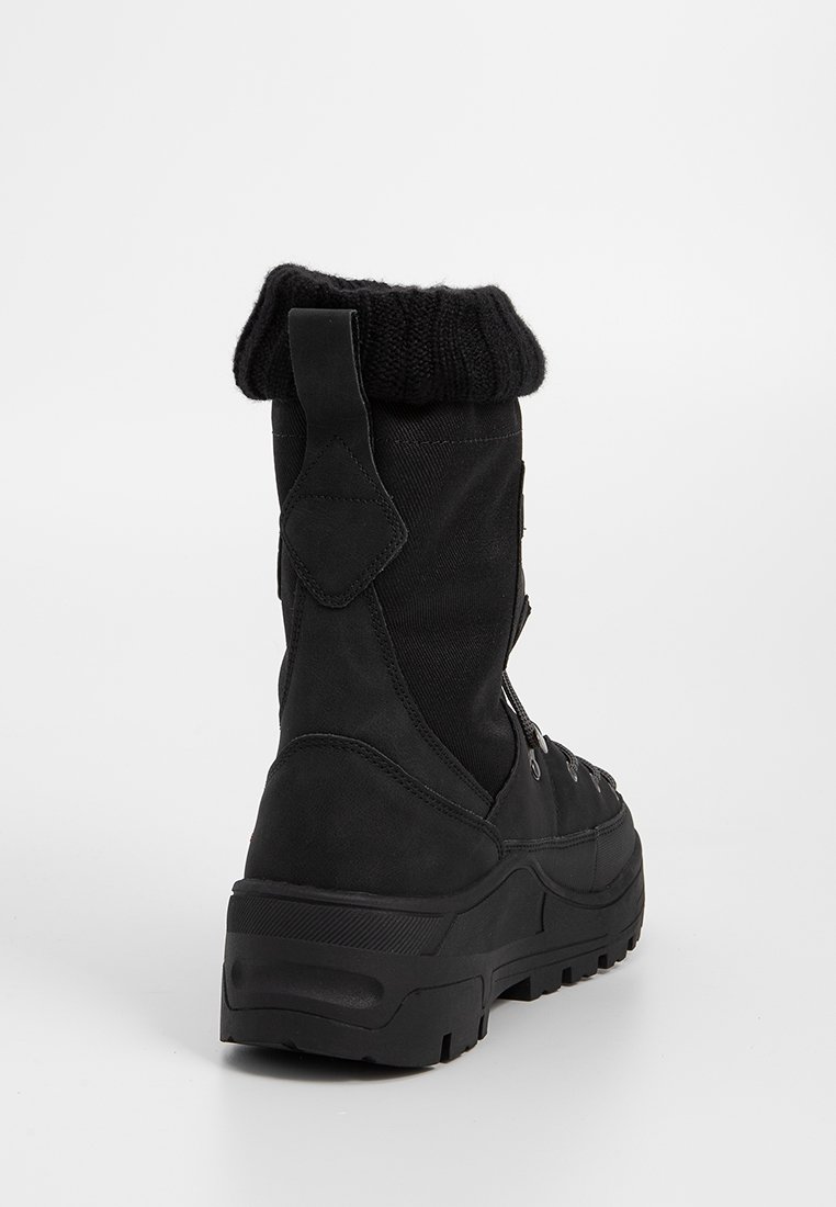 Zwarte enkelboot met een bovenwerk van textuurstof, gebreid been en een stevige rubberen zool. Voorzien van veters en een gewatteerde hak voor ondersteuning.