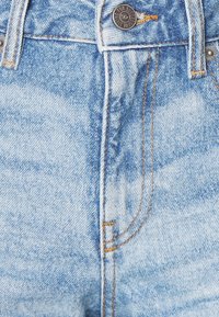 Vaaleansiniset farkut, joissa on haalistunut pinta, messinkiväriset ompeleet, metallinen nappisuljenta ja klassinen viiden taskun malli.