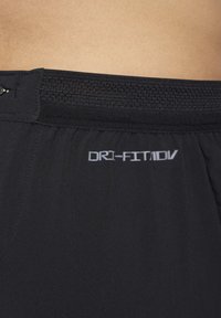Crne atletske kratke hlače s teksturiranim pojasom i reflektirajućim "DRI-FIT ADV" logotipom blizu rubova. Glatka tkanina s minimalnim detaljima šavova.