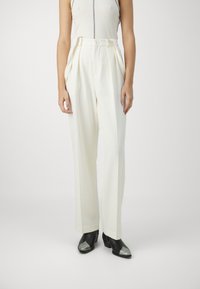 White, high-waisted trousers with pleats, featuring a smooth texture and a button closure. Paired with black shoes with silver accents.