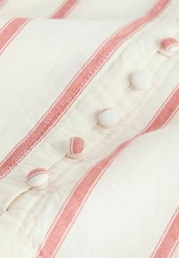 Gros plan sur un tissu blanc à rayures verticales roses avec des boutons recouverts de tissu alternant les rayures blanches et roses sur un vêtement.