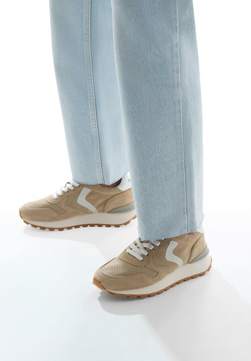 Beige sneakers med net og ruskind, med hvide akcenter og en skridsikker gummisål. Parret med lyseblå lige ben jeans.