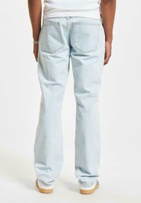 Blugi din denim decolorat cu un design drept. Au două buzunare pe spate și o croială lejeră. Completate cu adidași albi.