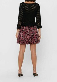 Schwarzer gestrickter Pullover mit langen Ärmeln und offenen Maschenmustern, kombiniert mit einem schwarzen und rosa blumenbedruckten Minirock. Schwarze High-Heels.