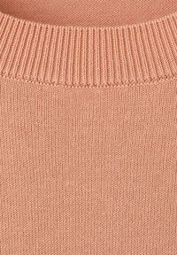 Zbliżenie na miękki różowy dzianinowy materiał z drobnymi pionowymi ściegami i prążkowanym brzegiem kołnierza.