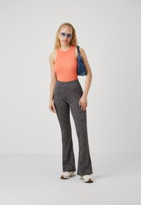 Orange ribbed tank top, black and white patterned flared pants, paired with a blue bag and cream sneakers. Transparent rectangular sunglasses.