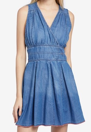 Niebieska sukienka z dżinsu bez rękawów z kopertowym dekoltem w kształcie litery V, dopasowaną talią i rozkloszowanym dołem, noszona przez kobietę od ramion do połowy uda.