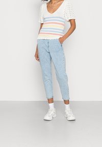 Hæklet top med multicolor vandrette striber, korte puffærmer; parret med lyseblå tapered jeans og hvide sneakers.
