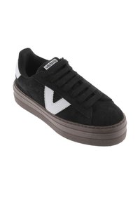 Zapatillas de ante negro con detalles de cuero, con un logotipo en forma de V blanco, puntera redonda, diseño de cordones y una suela gruesa de goma marrón.