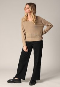 Beige V-hals trui van een zacht breigoed, gecombineerd met hoge zwarte wijde broek en zwarte veterschoenen. Eenvoudige ontwerpkenmerken.