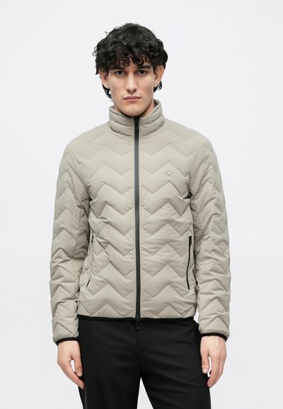 Világosszürke pufi dzseki magas gallérral, cikkcakkos steppelt mintával, elülső cipzárral és oldalsó cipzáras zsebekkel. Sima textúra, minimális márkajelzés.