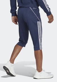 Navyblå träningsshorts i slitstark tyg med vita sidostråk och fickor med dragkedja, skurna till midjan på vaden. Vita sneakers.