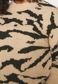 Primer plano de un suéter de punto beige con un patrón abstracto de rayas de tigre negro en una persona con cabello rizado.