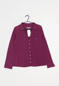Blusa viola a maniche lunghe con chiusura a bottoni, colletto, taschino sul petto e texture morbida, esposta su una gruccia.