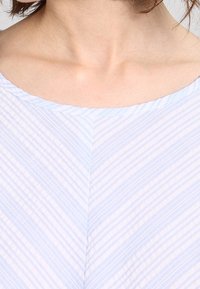 Helles blaues Oberteil mit einem Chevron-Muster und dünnen weißen Streifen. Der Stoff hat eine glatte Textur und einen weiten Ausschnitt.
