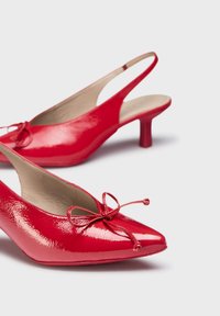 Escarpins slingback en cuir verni rouge avec un bout pointu, un détail en nœud à l'avant et un petit talon épais. Texture lisse sur toute la surface.