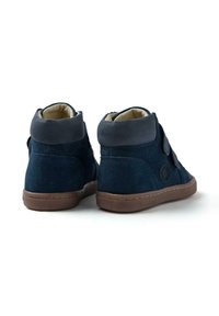 Zapatillas altas de ante azul marino con un collar de cuero gris, cinta de velcro y suela de goma marrón que presenta un detalle de logo circular en el lado.
