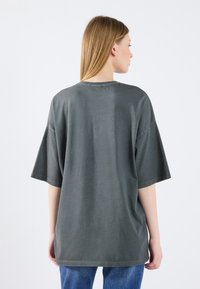 Oversized gray cotton t-shirt with short sleeves, round neck, and a smooth texture. Back view shows loose fit and minimal detailing.