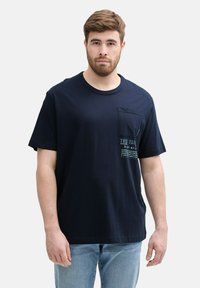 Granatowa bawełniana koszulka z okrągłym dekoltem, krótkimi rękawami i kieszonką na piersi z nadrukowanym tekstem i grafiką.