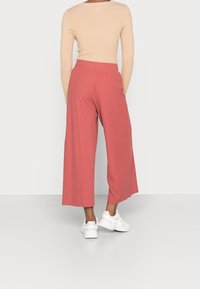 Haut à manches longues côtelé pâle associé à un pantalon large corail et des baskets blanches. Accent sur la coupe décontractée et les textures douces.