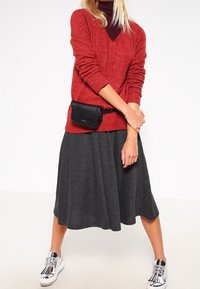 Un pull en laine rouge avec un col en V, associé à une jupe plissée gris foncé et des baskets argentées. La tenue comprend une petite ceinture noire.