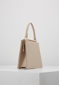 Beżowa torebka z sztucznej skóry o trójkątnym kształcie, z krótkim uchwytem, metalowymi akcentami i zapięciem na zamek. Gładka tekstura i minimalne detale szwów.