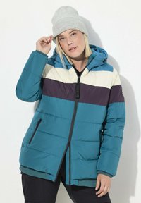 Giubbotto imbottito color turchese con strisce orizzontali viola e crema, chiusura con zip, due tasche laterali e cappuccio. Indossato con un berretto grigio chiaro.