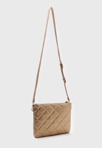 Vadderad beige axelväska med justerbar rem och dragkedjestängning. Slät yta med diamantmönster på framsidan. Rektangulär form.