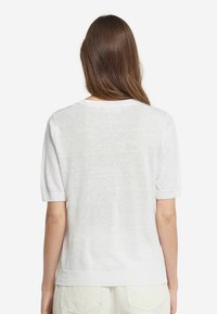 Hvid strikket sweater med korte ærmer og ribbede manchetter. Blød tekstur med et let design, der har en rund halsudskæring og afslappet pasform.