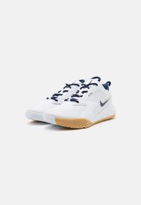 Witte sportschoenen met marineblauwe accenten, een textuur rubberen outsole en mesh panelen. Voorzien van een prominent Nike-logo aan de zijkant en platte veters.