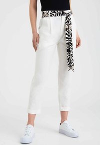 Białe spodnie z podwiniętym dołem, z czarno-białym paskiem w zwierzęcy wzór zebry. Połączone z białymi trampkami.