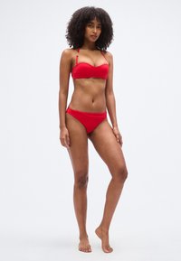 Σετ κόκκινου μπικίνι με τοπ χωρίς τιράντες και ρυθμιζόμενες τιράντες ώμου και χαμηλόμεσο στρινγκ, κατασκευασμένο από λείο, ελαστικό ύφασμα.