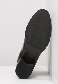 Černá kožená bota s hladkým povrchem, vybavená plochou, textura gumovou podrážkou. Velikost boty 37 je uvedena na boku.
