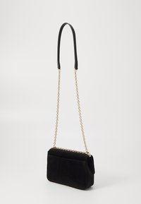 Sac à bandoulière en suède noir avec une courte poignée en cuir et une bandoulière en chaîne dorée, présentant une forme rectangulaire et un détail de poche arrière.