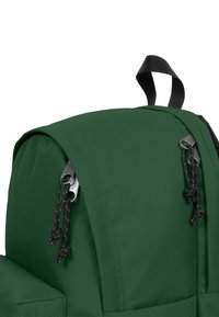 Mörkgrön ryggsäck med en slät tygyta, med en övre lucka, svarta detaljer i metall och svarta dragsnören på dragkedjan.