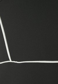 Tecido preto com uma textura suave e detalhes em costura branca, apresentando um padrão geométrico criado por linhas contrastantes.