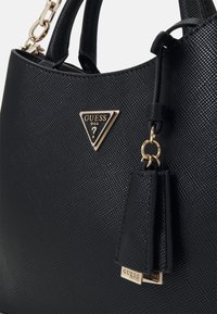 Borsa a mano nera con struttura rigida in materiale sintetico testurizzato, con accessori in argento, badge logo triangolare e charm attaccato con il nome del marchio.