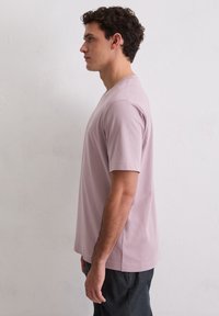 Világos mályvarózsaszín, rövid ujjú póló, puha pamutból készült, környakú és laza szabású, sötét nadrággal viselve.