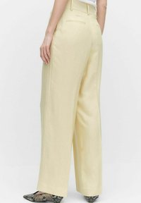 Pantalons larges en tissu jaune clair, avec une texture lisse, deux poches arrière et une taille haute.