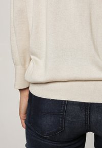 Krémový pletený svetr s volným střihem, žebrovanými manžetami a lemem. Spárovaný s tmavými džínami s klasickým designem zadní kapsy.