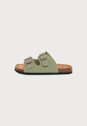 Offene Sandale mit hellgrünen, gesteppte Riemen, zwei verstellbare Schnallen, Kork-Fußbett und schwarzer Sohle, von der Seite gezeigt.