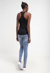 Musta ilmanhiha tankkitoppi, jossa on tiukka muotoilu, yhdistettynä vaaleansinisiin skinny-farkkuihin ja valkoisiin tennareihin. Saumaton kangas ja rento istuvuus.