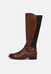 Brown leather knee-high boot with ribbed black material on the side, silver buckle detail, round toe, and a low heel.