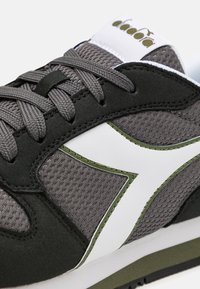 Sneaker con una parte superiore in mesh grigio testurizzato, accenti in suede nera, un logo bianco e dettagli verdi di lato, con lacci grigi.