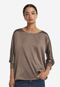 Top in satin marrone con scollatura ampia, maniche a 3/4 e vestibilità rilassata, caratterizzato da una texture liscia e dettagli di cucitura minimali.