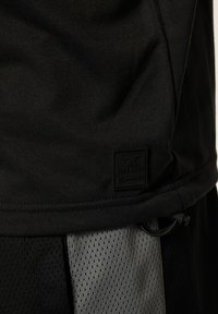 Camiseta deportiva negra con un tejido texturizado y un parche con el logo. El diseño incluye un panel de malla negra y gris sólido para mejorar la transpirabilidad.