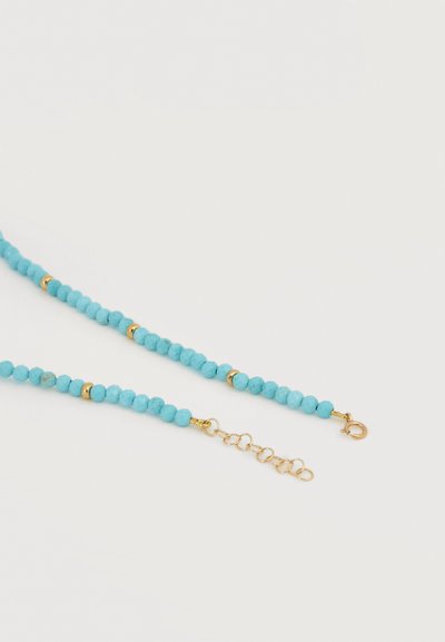 Κολιέ με τιρκουάζ χάντρες και μικρές χρυσές διαχωριστικές χάντρες, με χρυσό αλυσιδάκι προέκτασης σε λευκό φόντο.