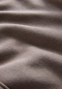 Tejido suave y tejido en un color topo suave con una textura lisa y un ligero estiramiento, mostrando suaves caídas y curvas.